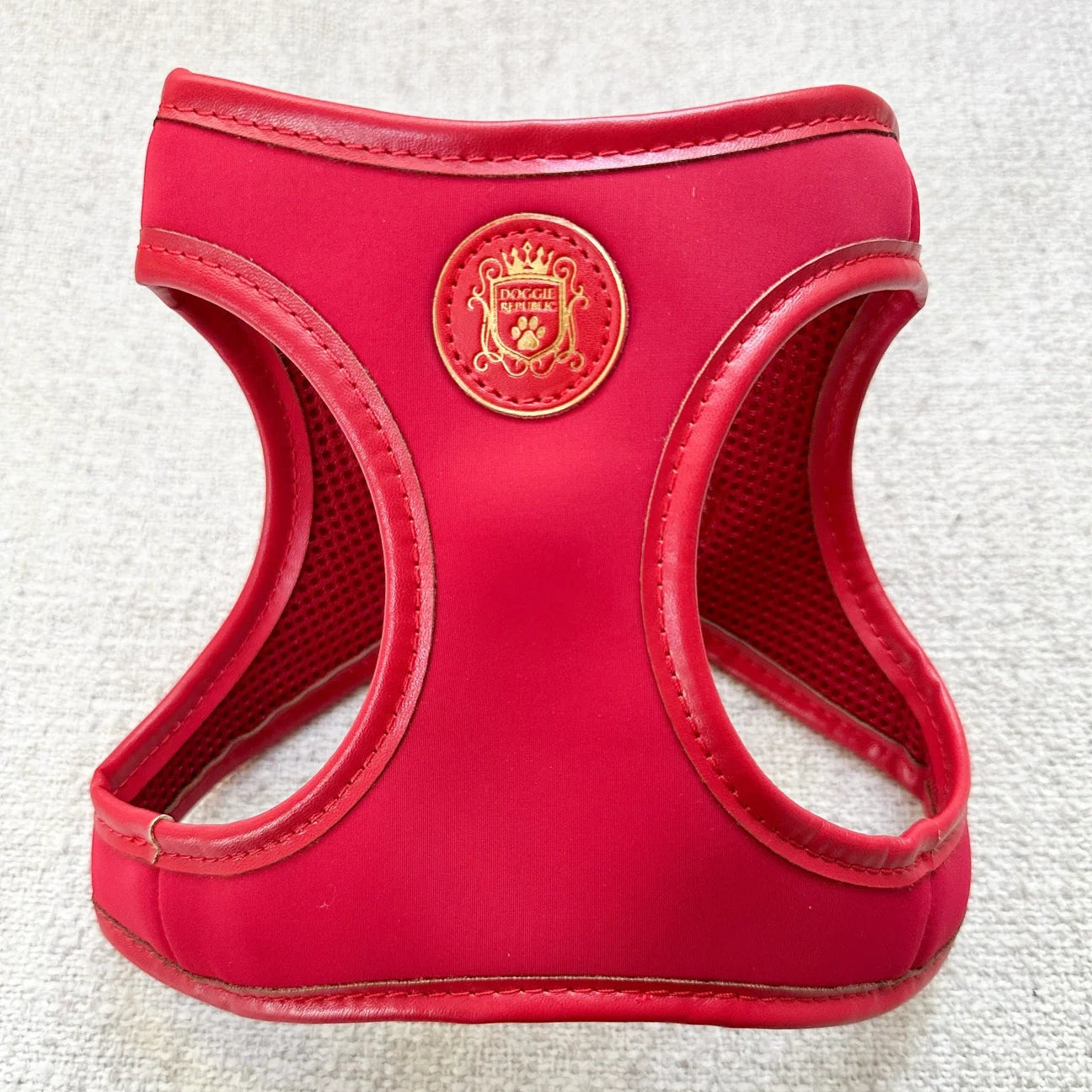 Red pet harness with a gold emblem on a textured white background